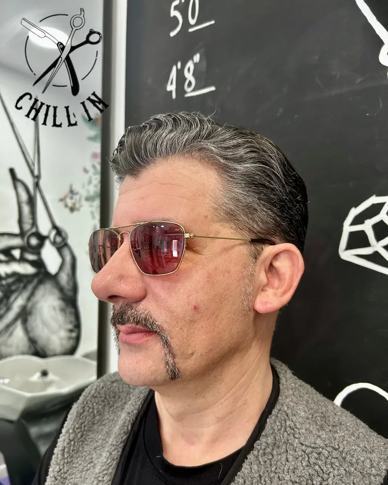 Uomo con baffi curati e capelli pettinati all'indietro